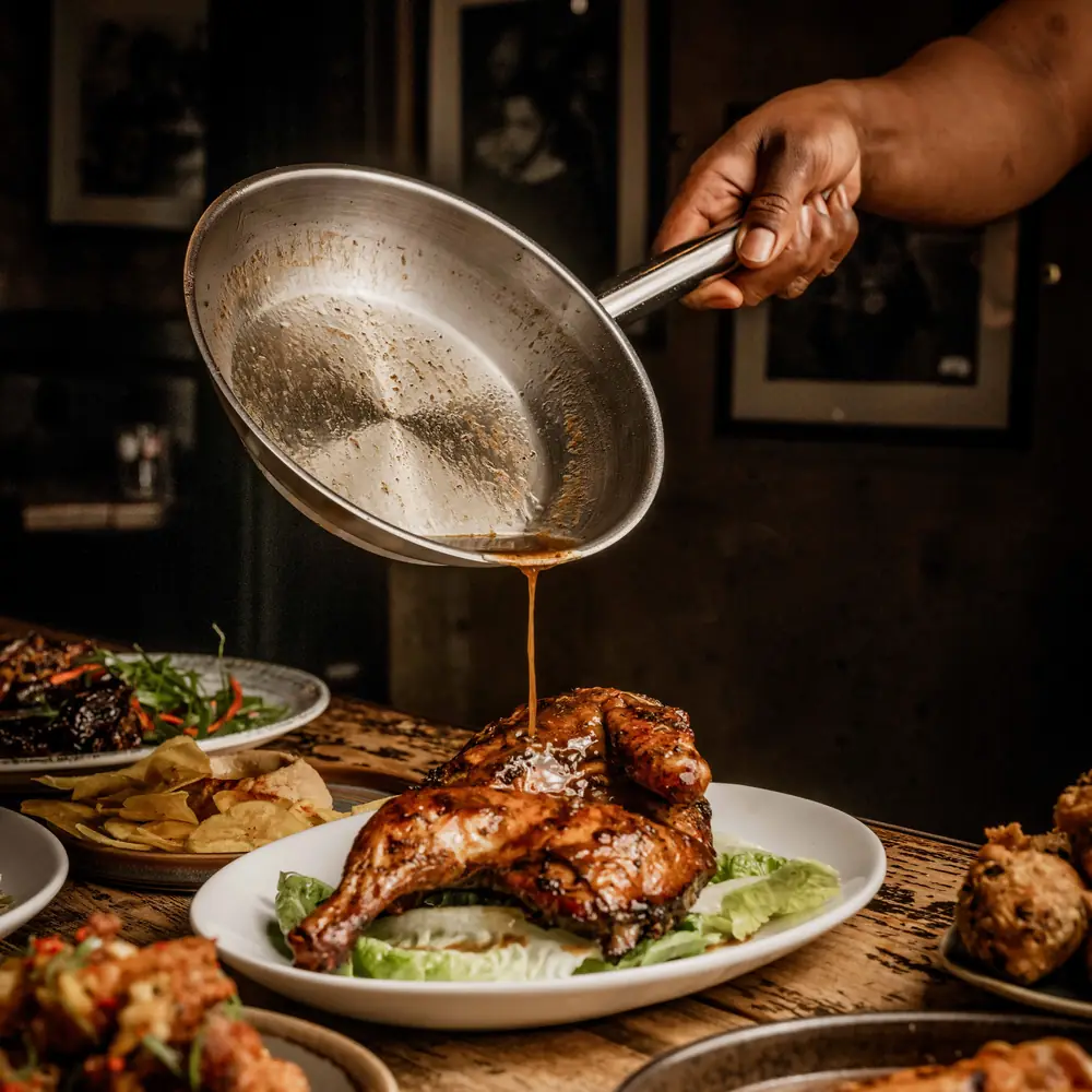 Jerk sauce being poured over half a jerk chicken at Likkle Bit